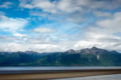 A wide panoramic view of Turnagain Arm in Alaska, with dark green mountains and a dramatic, cloudy sky.